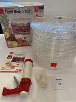 Full overview showing the Ronco Food Dehydrator with its box, five drying trays stacked on the base unit, jerky gun, accessories, and manuals on a white surface.