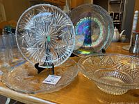 Photo showing two clear glass bowls and two glass trays on a wooden table. One bowl has iridescent coloring. A floral etched tray is visible with a chip.