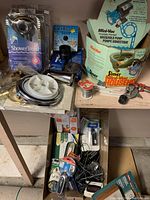 Lot overview on shelf showing a variety of plumbing and electrical items including the boxed household pump and boxed shower hose.