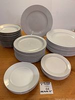Stacked white plates with some featuring thin gold rim and large flat charger plates behind
