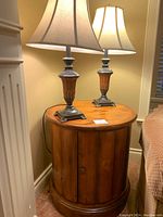 Two table lamps on top of round wood storage cabinet, showing overall appearance and size.