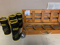 Four metal bocce balls in OBUT branded black soft zippered cases with yellow trim, placed next to a wooden box of metal horseshoes and one loose bocce ball.