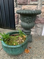 Green urn and round pot placed side by side outdoors on cement surface near stone wall