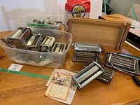 Pasta maker parts including several metal rollers and cutters, a wooden rolling board, and a plastic container with more pieces. Also visible a bag of Rogers flour in the background.