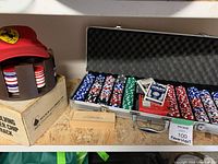 Photo showing the metal carrying case open with organized poker chips and playing cards inside, a Ferrari chip holder on left, and a wooden domino box beneath the items on plywood surface.