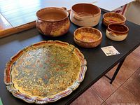 Overall view of the five pottery bowls and decorative tray on a black folding table showing color and design variety