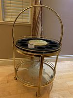 Front view of brass rolling bar cart with glass shelf and black tray top with circular slots.