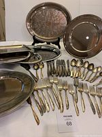 Full view of set showing flatware forks, spoons arranged with large serving plates mostly round with some oval and rectangular trays