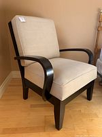 Full view of beige ultra suede cushioned stylus chair with dark wood base and curved armrests positioned on wooden floor.