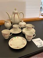 Full view of the tea set showing tea pot, sugar bowl with lid, creamer, four cups, and four saucers with floral and gold design on white ceramic.