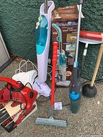 Photo showing the complete lot outside against a green wall including the StreamTek steam mop with water reservoir, hand vacuum, carpet sweeper, mop, and plunger.