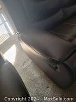 Side view showing brown leather upholstery and power recline button on armrest, with visible stitching and good condition.