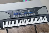 Front angled view of Techno-Beat electronic keyboard piano showing 49 keys, control buttons, built-in speakers, and stand.