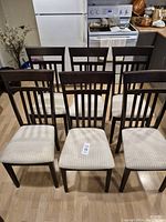 Six wooden dining chairs with light fabric seats arranged in two rows on a kitchen floor.