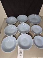 Set of nine light blue/grey scalloped edge bowls displayed together on brown backdrop.