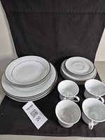 Full view of the 18 piece bone china dinner set arranged including plates, bowls, cups, and saucers. White bone china with silver edging visible on all items.