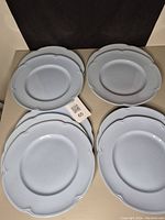 Set of four scalloped edge grey dinner plates stacked in two piles, showing size and shape.