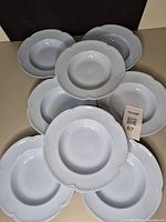 Eight grey-blue scalloped edge rimmed soup bowls arranged with one central and others around