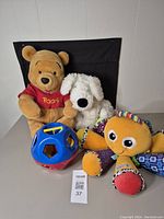 Full view of the lot shows a Winnie the Pooh plush, white dog plush, Lamaze musical octopus, and shape sorter toy.