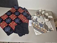 Six batik style placemats with geometric patterns and four black napkins arranged on a table beside six bird motif napkins rolled and held with ceramic napkin rings.