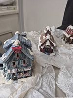 Photo showing front view of three winter-themed ceramic buildings including a Christmas shop and two houses with snow accents.