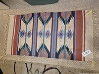 Full view of the rug laid flat on a light carpet floor showing the complete pattern and fringes.