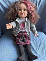 Photo of the doll showing curly brown hair with pink streak, green eyes, dressed in gray blazer, white shirt with heart design, plaid skirt, and black tights.