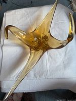 Top-down photo of a vintage hand-blown art glass centrepiece in amber, showing its three elongated pointed arms and fluid abstract shape on a white cloth.