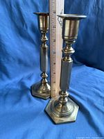 Pair of brass candleholders standing against a blue cloth background with a ruler showing approximately 8 inches height