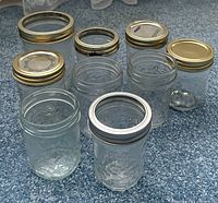 Top view of eight glass canning jars with assorted gold and silver lids placed on carpet.