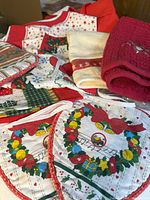 Photo showing an assortment of Christmas-themed kitchen towels and pot holders with festive designs including wreaths, musical notes, and red textured fabric.