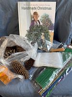 Image of crafting lot with Martha Stewart Handmade Christmas book, pinecones, pipe cleaners in green and blue, small orange beads, wooden-handled tool, and clear plastic bags.