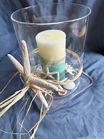 Tall clear cylindrical hurricane lamp with beach-themed candle and seashell base