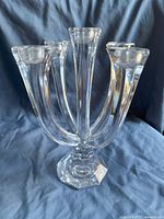 Photo of a clear glass candelabra centerpiece showing five curved arms each with a candle holder and a multi-faceted geometric base on a blue cloth background.