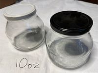 Photo of two empty clear glass containers with screw-on lids, one white and one black, labeled 10 oz.