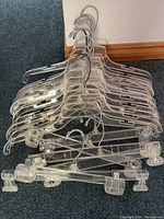 A collection of 25 clear acrylic hangers with metal hooks, including both shirt and pant/skirt designs, arranged stacked together.