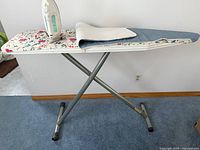 Photo of the ironing board set up with iron placed on its rest and two separate ironing pads folded on the board.