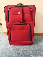 Front view of a red soft-sided suitcase with multiple zippered compartments and adjustable strap.