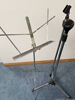 Metal sheet music stand and black microphone stand against white wall and wooden floor