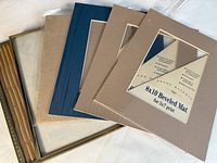Photo showing assortment of picture frames and beveled mats in neutral colors including beige, brown and navy blue.