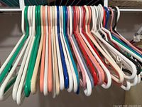 Photo shows an assortment of about 25 sturdy plastic clothes hangers in various colors hanging on a closet bar.