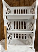 Photo of three white plastic stacking storage bins, shown stacked vertically with a wooden ruler beside them for scale.