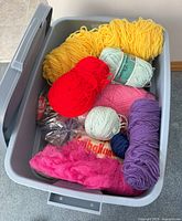 Open Rubbermaid plastic tote filled with multiple skeins and balls of yarn in assorted bright colors including yellow, red, pink, purple, mint green, white and navy blue.