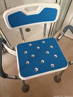 Shower chair with blue seat and backrest, metal legs, and rubber tips shown in a bathroom setting.