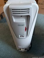 Front view showing the DeLonghi logo, the control dial, and base wheels of the white electric radiator-style space heater.