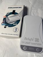 Photo of white BeSafe UV Light Sanitizer Sterilization Box with original packaging box on white fabric background.