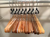 Photo showing nine wooden pant hangers lined up on a clothing rod, showcasing their design and condition.