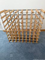 Wooden wine rack standing on carpeted floor showing grid structure for holding wine bottles