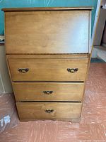 Front view of closed wooden writing desk showing three drawers with metal handles.