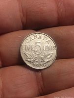 Reverse side of the 1928 Canadian 5 cent coin showing the value, maple leaf design and date 1928.